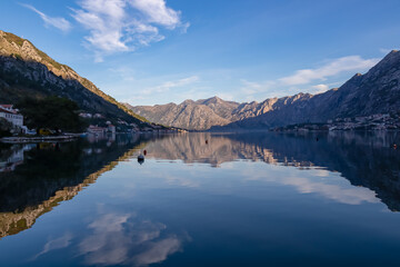 Panoramic view of bay of Kotor at sunrise in summer, Adriatic Mediterranean Sea, Montenegro, Balkans, Europe. Fjord winding along coastal towns. First sunbeams on Lovcen mountains. Water reflection