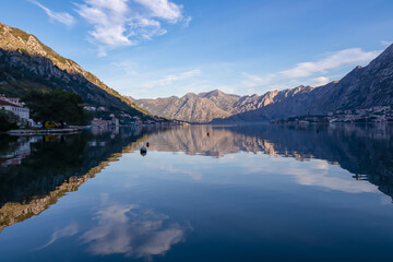 Fototapeta premium Panoramic view of bay of Kotor at sunrise in summer, Adriatic Mediterranean Sea, Montenegro, Balkans, Europe. Fjord winding along coastal towns. First sunbeams on Lovcen mountains. Water reflection