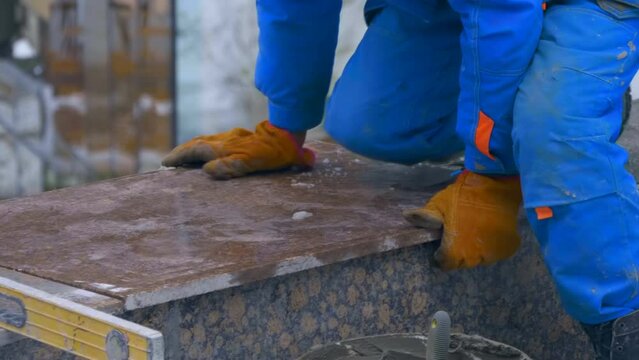 A worker lays on cement mortar and fine-tunes polished granite facing slab in a huge beautiful building complex under construction with glass fasade