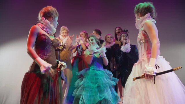 Portrait of excited character throwing away jacket clapping as two princesses start swords fight on stage. Talented Caucasian men and women playing modern fairytale performance in theater