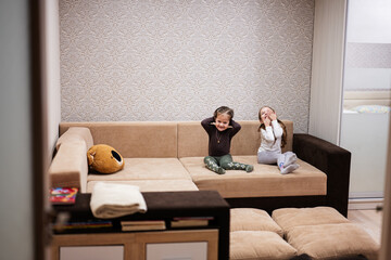 Two sisters at home on the sofa laughing loudly together.