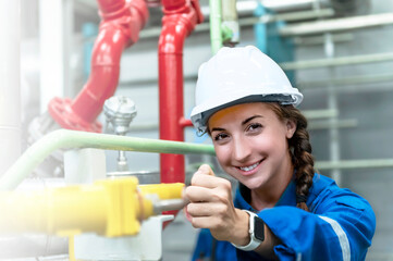A female engineer inspects the work inside the factory while smiling and wearing a white hard hat.