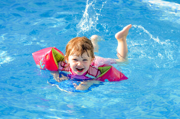 Beautiful young girl playing in the pool with her arm bands