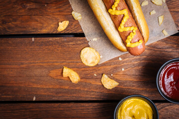 Classic fast food hot dog served with mustard on a rustic wooden board. Served with potato chips and sauces. 