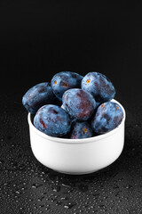 A handful of blue plums in a white plate on a dark background.