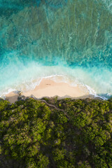 View from above, stunning aerial view of a person wlking on a beautiful beach bathed by a turquoise rough sea at sunset, Green Bowl Beach, South Bali, Indonesia..