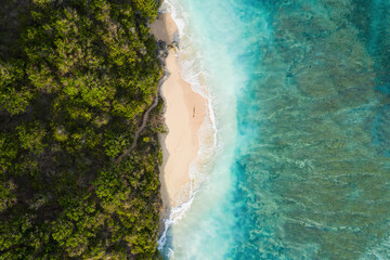 View from above, stunning aerial view of a person wlking on a beautiful beach bathed by a turquoise rough sea at sunset, Green Bowl Beach, South Bali, Indonesia..