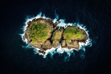 View from above, stunning aerial view of a little rocky island bathed by a rough sea at sunset....