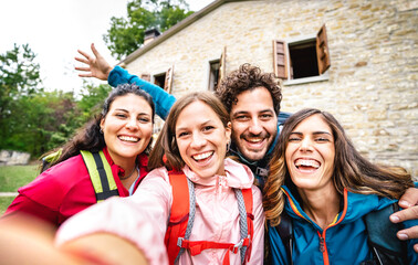Young people group taking selfie at trekking excursion by countryside cottage - Sporty life style concept with happy millenial friends having fun together at camping experience - Bright cloudy filter