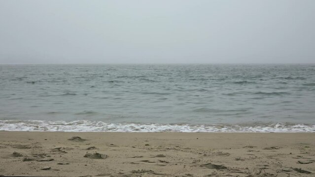 The ocean shore in heavy fog without people. The waves of the ocean move calmly.