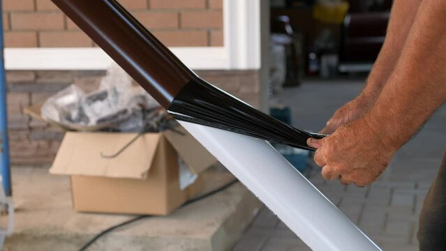 Removing the protective film from the new gutter before installation. Installation of the drainage system. Construction of a private house.