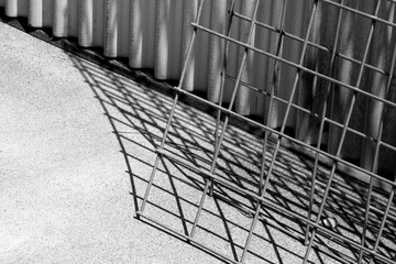 Closeup of industrial steel wall and wire fencing in black and white, with shadows.