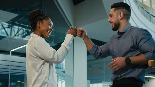 Diverse multiracial friendly business partners colleagues African American woman with Arabian Indian man talking in office hit with fists power five respect friendship partnership support gesture