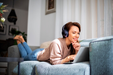Attractive woman relaxing at home and using earphone and laptop