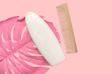 White shampoo lies on a pink palm leaf. And a wooden comb.