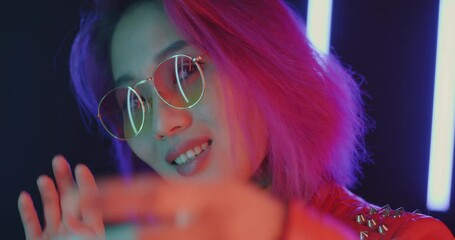 Close-up portrait of carefree Asian student dancing moving hands in neon illuminated night club. Young lady enjoying music and leisure time.