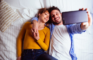 Obraz premium young couple relaxing in bed and having fun. Taking selfies during vacation in the bedroom