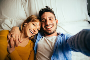 young couple relaxing in bed and having fun. Taking selfies  during vacation in the bedroom