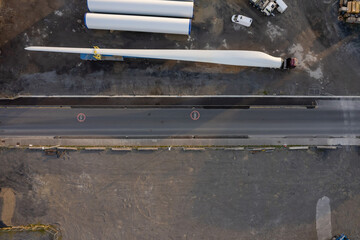 Huge size wind turbine blade on a platform ready for transportation in a yard. Aerial view. Heavy and long cargo movement. Building green energy source.