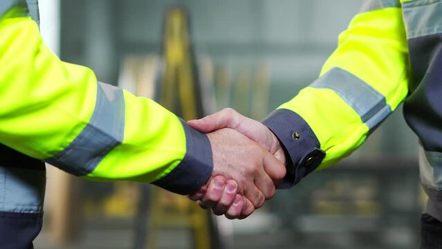 Close up of Caucasian men shaking hands at factory as sign of agreement and good work together. Inside. Males constructors or builders shake hands. Gesture of agreeing of two workmen at manufactory.