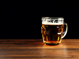 Glass of lager beer on a brown wood table. Dark background. Alcohol consumption. Dark background.