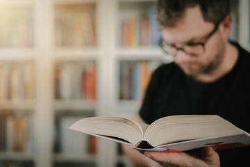 Man holding an open book. Man is reading book. Blurred books in background.