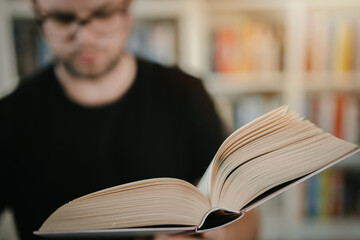 Man holding an open book. Man is reading book. Blurred books in background.
