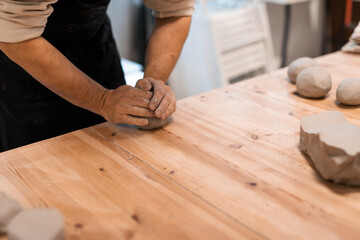 Kneading piece of raw grey clay by man hands on wooden table. DIY potter hobby