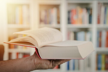 Man holding an open book. Man is reading book. Blurred books in background.