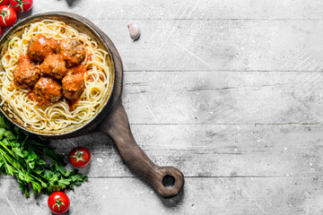 Pasta and meat balls in pan with parsley and tomatoes.