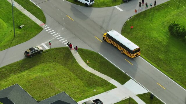 Aerial view of american yellow school bus picking up children at sidewalk bus stop for their lessongs in early morning. Public transportation in the USA