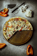 on a black background there is a pizza on a board, scattered flour, pepper, mushrooms and utensils; sliced ​​pizza; not a whole pizza on the board; pieces of pizza on the table