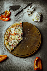 on a black background there is a pizza on a board, scattered flour, pepper, mushrooms and utensils; sliced ​​pizza; not a whole pizza on the board; pieces of pizza on the table