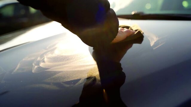 Slow-motion close up male's hand with foam sponge washing car windshield with morning sunlight. Car cleaning and detailing concept.