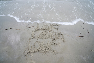 Live Laugh Love phrase written on the beach in the sand as the ocean waves roll in