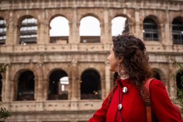 Fototapeta na wymiar Woman in red coat looking from outside the Roman Colosseum, in Rome, in Italy