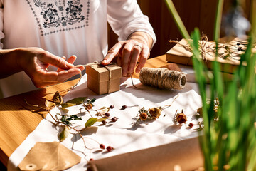 Woman decorating wrapped gifts with recycled paper with dried flowers. Natural aesthetic. Zero waste, plastic free, trendy, handmade gift package.