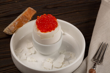 Boiled egg partially peeled from the shell in a stand, red caviar on top