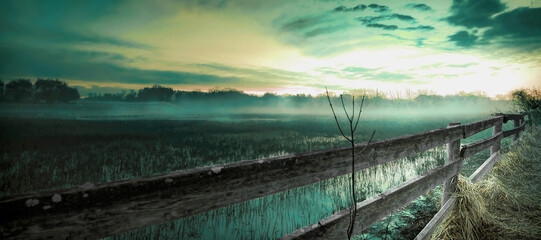 Moody foggy farm field with wooden fence