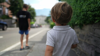 Fototapeta na wymiar Little boy walking on city sidewalk. Toddler walks outside playing