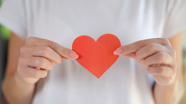 Woman holds heart in her hands in front of her chest.