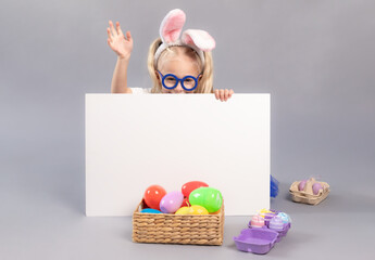 Little girl hiding behind white board over gray background. Child wearing bunny ears. Easter concept. Space for design