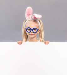 Kid wearing bunny ears, standing behind white board over gray background. Easter concept image. Space for design