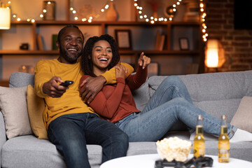 Joyful african american couple watching TV together at home - obrazy, fototapety, plakaty