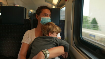 Mother holding baby toddler traveling by train wearing covid face mask during pandemic
