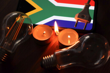 Loadshedding concept scene. Candles, lightbulbs and plug in front of the South African flag....