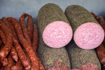 Sausage and others meat smoked delicacies of different colors and sizes are stacked on counter. Fair trade in homemade meat delicacies. Close-up. Selective focus.