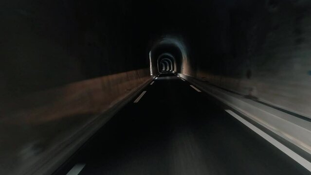 Vehicle perspective of car traveling inside dark tunnel gallery. Concept of automobile or truck driving in dark freeway during a journey. Light in background. Auto trip on the road