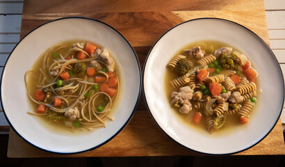 Top view of two chicken noodle types on natural wood surface