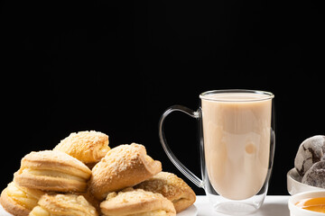 Tea with milk in a glass cup with a double bottom and cakes on a black background, place for text